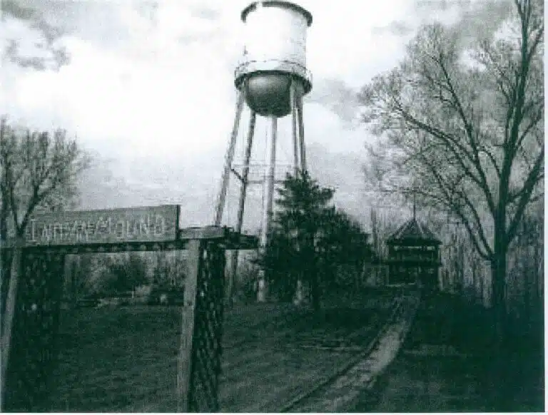 Photo with caption: Not the clearest image, but one we are lucky to have in the Laurel Library’s collection. From left to right one can see the park entrance sign that said “Indian Mound,” the old water tower, and the bandstand on top of the mound.